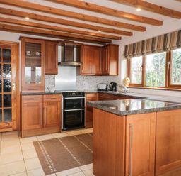 A kitchen with wooden cabinets a stove a window with striped blinds and a wooden door at Lynton House in Ruardean Hill near Drybrook