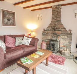 A living room with a brown couch and cushions a wooden coffee table books a stone fireplace a television and a lamp at Lynton House in Ruardean Hill near Drybrook