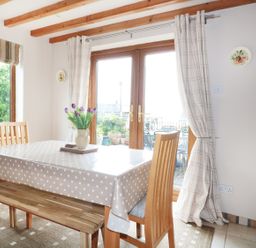A dining area with a wooden table covered with a polka dot tablecloth and wooden chairs near glass doors at Lynton House Ruardean Hill near Drybrook
