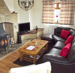 A living room with a stone fireplace a leather sofa with red cushions a wooden coffee table and a television at Hartam House in Falstone near Kielder and Bellingham