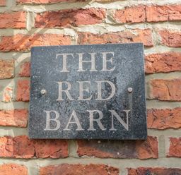 A black stone plaque with the words The Red Barn mounted on a red brick wall at The Red Barn in Longframlington near Alnwick