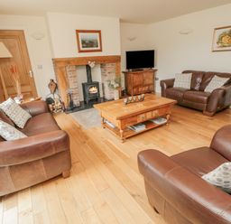 A living room with brown leather sofas a wooden coffee table a fireplace and a television at The Red Barn in Longframlington near Alnwick