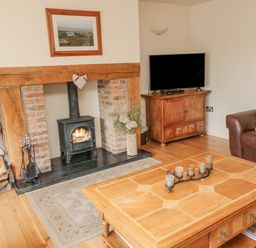 A living room with a fireplace a wood stove a wooden coffee table and a television at The Red Barn in Longframlington near Alnwick