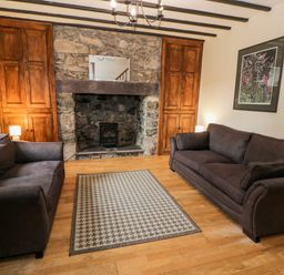 A living room with two dark sofas a stone fireplace wooden cabinets and a patterned rug at Ddol Helyg Farmhouse Llanrug