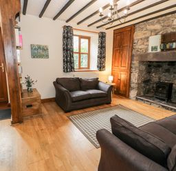 A living room with two sofas a fireplace a wooden door and window at Ddol Helyg Farmhouse Llanrug