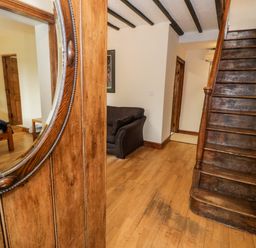 A wooden staircase next to a brown sofa and a wooden door with a round mirror at Ddol Helyg Farmhouse Llanrug