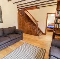 A living room with two couches a patterned rug a wooden staircase and a bookshelf at Ddol Helyg Farmhouse Llanrug