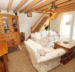 A living room with floral sofas a wooden coffee table a wooden dining table a wooden cabinet and stairs at Morfa Isaf Cottage in Llangrannog