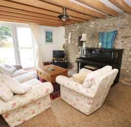 A living room with floral sofas a wooden coffee table a piano and exposed stone wall at Morfa Isaf Cottage in Llangrannog