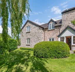 A stone house with windows surrounded by a lawn and bushes with a tree hanging in front at Distyll in Llanfwrog near Ruthin