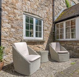 Two outdoor wicker chairs with cushions and a small table between them outside a stone wall house at Distyll Llanfwrog near Ruthin
