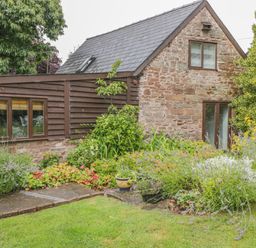 A garden with various plants and flowers in front of a stone and wood cottage at Pembridge Cottage in Welsh Newton