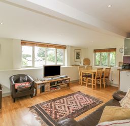 A living room with leather chairs a television wooden dining table and kitchen appliances at Pembridge Cottage in Welsh Newton