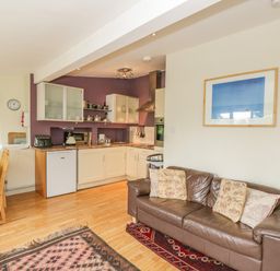 An open kitchen and living area with a brown leather sofa and dining table at Pembridge Cottage in Welsh Newton