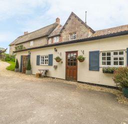 A cottage exterior with blue shuttered windows wooden doors flower baskets and a gravel path at Colly Cottage in Dottery