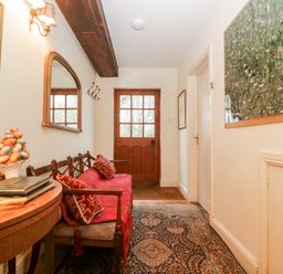 A hallway with a wooden bench with red cushions a wooden side table a wall mirror a map and a wooden door at Colly Cottage in Dottery