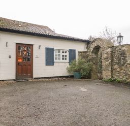 An outdoor area with a white building featuring a wooden door and blue shutters next to a stone archway at Colly Cottage in Dottery