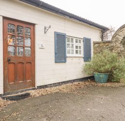 An entrance door and window with shutters on a white wall near a stone arch and potted plant at Colly Cottage in Dottery