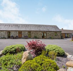 A stone building with wooden doors and windows surrounded by shrubs and rocks at Ysgubor Hir in Pontarddulais near Swansea