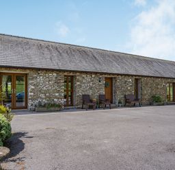 Stone building with wooden doors and windows two brown chairs and benches outside at Ysgubor Hir in Pontarddulais near Swansea