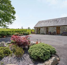 A stone building with wooden doors and windows and garden shrubs in the foreground at Ysgubor Hir in Pontarddulais near Swansea