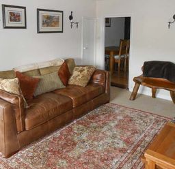 A living room with a leather sofa and wooden chair with cushions and a patterned rug at Tuckermarsh Quay River Cottage 2 Bere Alston near Tavistock