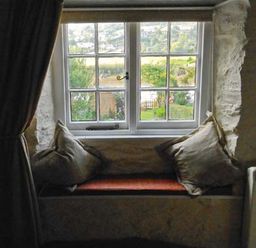 A window seat with cushions and a view of a garden through a window at Tuckermarsh Quay River Cottage 2 Bere Alston near Tavistock