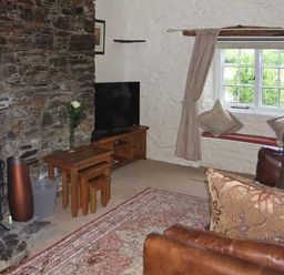 A living room with a stone fireplace a television a window seat with cushions and wooden furniture at Tuckermarsh Quay River Cottage 2 Bere Alston near Tavistock
