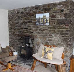 A room with a stone fireplace wood burning stove armchair with ottoman and wooden bench with cushions at Tuckermarsh Quay River Cottage 2 Bere Alston near Tavistock