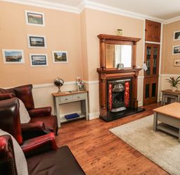 A living room with leather armchairs a fireplace a coffee table and framed pictures on the walls at Coquet Cottage in Amble