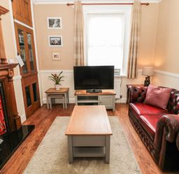 A living room with a leather sofa a coffee table a television and a fireplace at Coquet Cottage in Amble