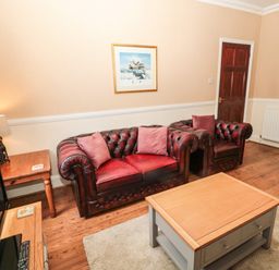 A living room with red leather sofas wooden coffee and side tables and a television at Coquet Cottage in Amble