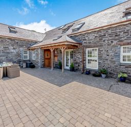 A stone exterior building with outdoor seating on a paved courtyard at Ysgubor Uchaf in Brongest near Newcastle Emlyn