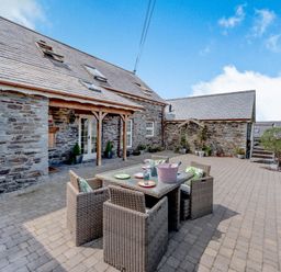 A patio with a dining table and chairs outside a stone building at Ysgubor Uchaf in Brongest near Newcastle Emlyn