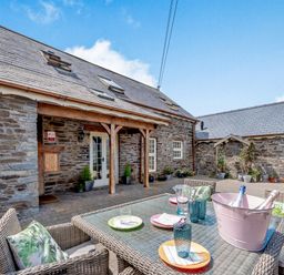 An outdoor patio with stone walls several skylights and a table set with plates glasses and a bucket of bottles at Ysgubor Uchaf in Brongest near Newcastle Emlyn