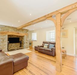 A living room with leather sofas a stone fireplace wooden beams and hardwood floor at Ysgubor Uchaf in Brongest near Newcastle Emlyn