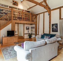 A living room with wooden beams bookshelves a TV on a cabinet sofas a coffee table and a staircase at Ducksfoot Barn Bush Green near Pulham Market
