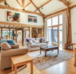 A living room with two sofas a wooden coffee table and large windows at Ducksfoot Barn Bush Green near Pulham Market