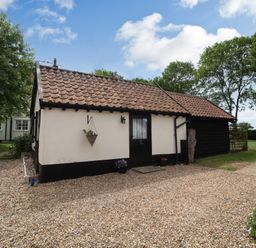 A single-story cottage with tiled roof gravel driveway and surrounding trees at Garden Cottage in Bush Green near Pulham Market