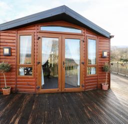 A wooden cabin with glass doors and windows on a wooden deck with potted plants at The Four Oaks Chalet in Blaich near Fort William