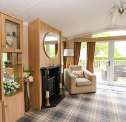 A living room with a beige armchair and fireplace next to glass doors and windows at The Four Oaks Chalet in Blaich near Fort William