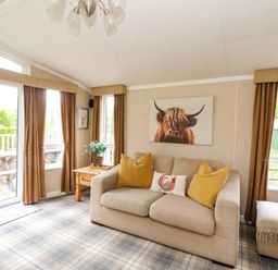 A living room with a beige sofa and yellow cushions a wooden side table and windows with brown curtains at The Four Oaks Chalet in Blaich near Fort William