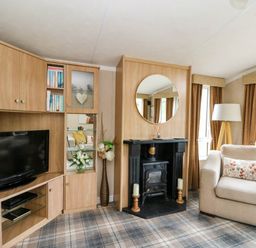 A living room with a television unit a fireplace with a round mirror and an armchair at The Four Oaks Chalet in Blaich near Fort William