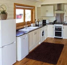 A kitchen with white cabinets appliances a brown rug and a window with wooden frame at Cropvale Lodge in Cropthorne near Pershore