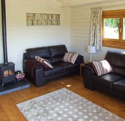 A sitting room with two black leather sofas a wood burning stove and a window with curtains at Cropvale Lodge Cropthorne near Pershore