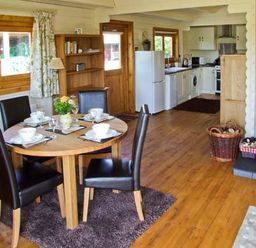 A dining area with a round table set for four next to a kitchen with white appliances and wooden floors at Cropvale Lodge in Cropthorne near Pershore