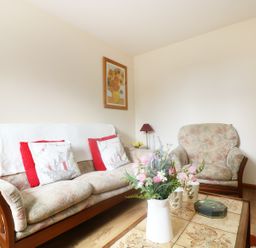 A living room with floral sofas a coffee table with flowers and cups and a painting on the wall at The Old Granary in Polyphant near Launceston