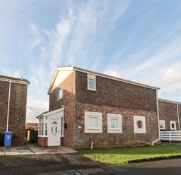 A two-story brick house with white framed windows and a white front door with a small front garden at Cheviot View in Beadnell