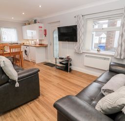 A living area with black leather sofas a wall-mounted TV wooden dining table and chairs and a kitchen with white cabinets at Cheviot View in Beadnell