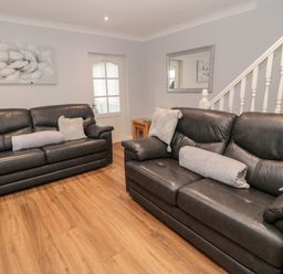 A living room with two black leather sofas wooden floor a side table a mirror a door and staircase at Cheviot View in Beadnell
